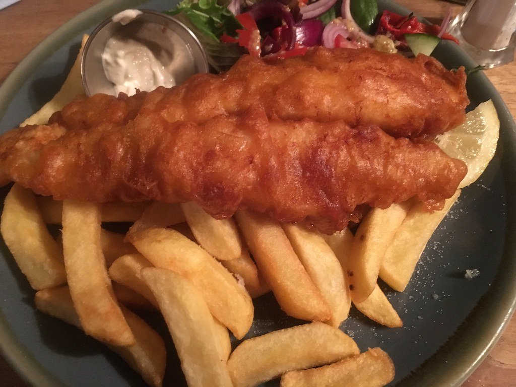 A portion of golden battered fish with thick-cut chips