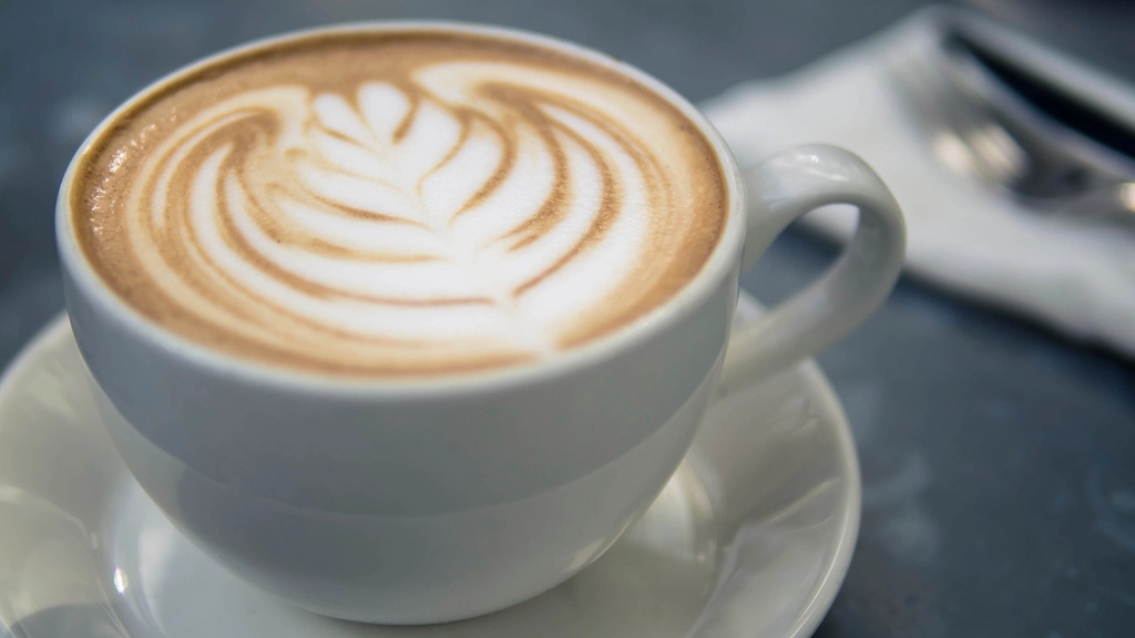 A cappuccino in a white cup with a detailed leaf pattern in the latte art