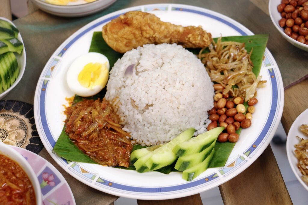 A plate of nasi lemak with rice, fried chicken, boiled egg, peanuts, cucumber and sambal on a banana leaf