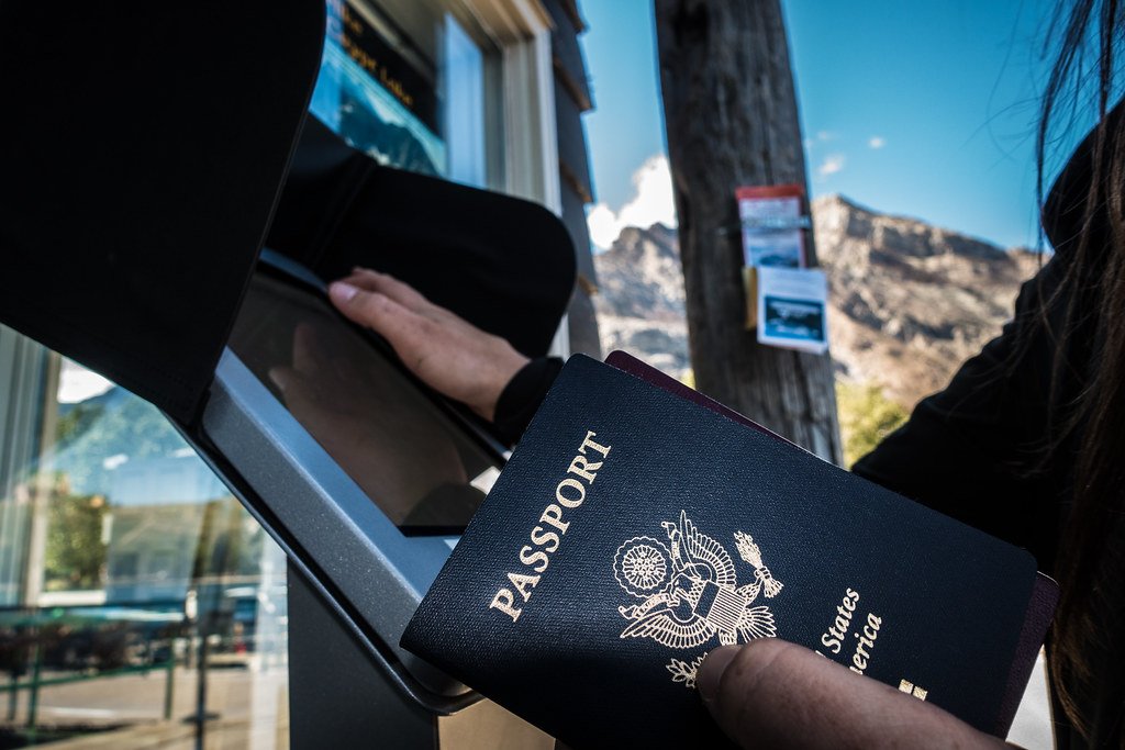A hand holding an open passport at a border crossing window